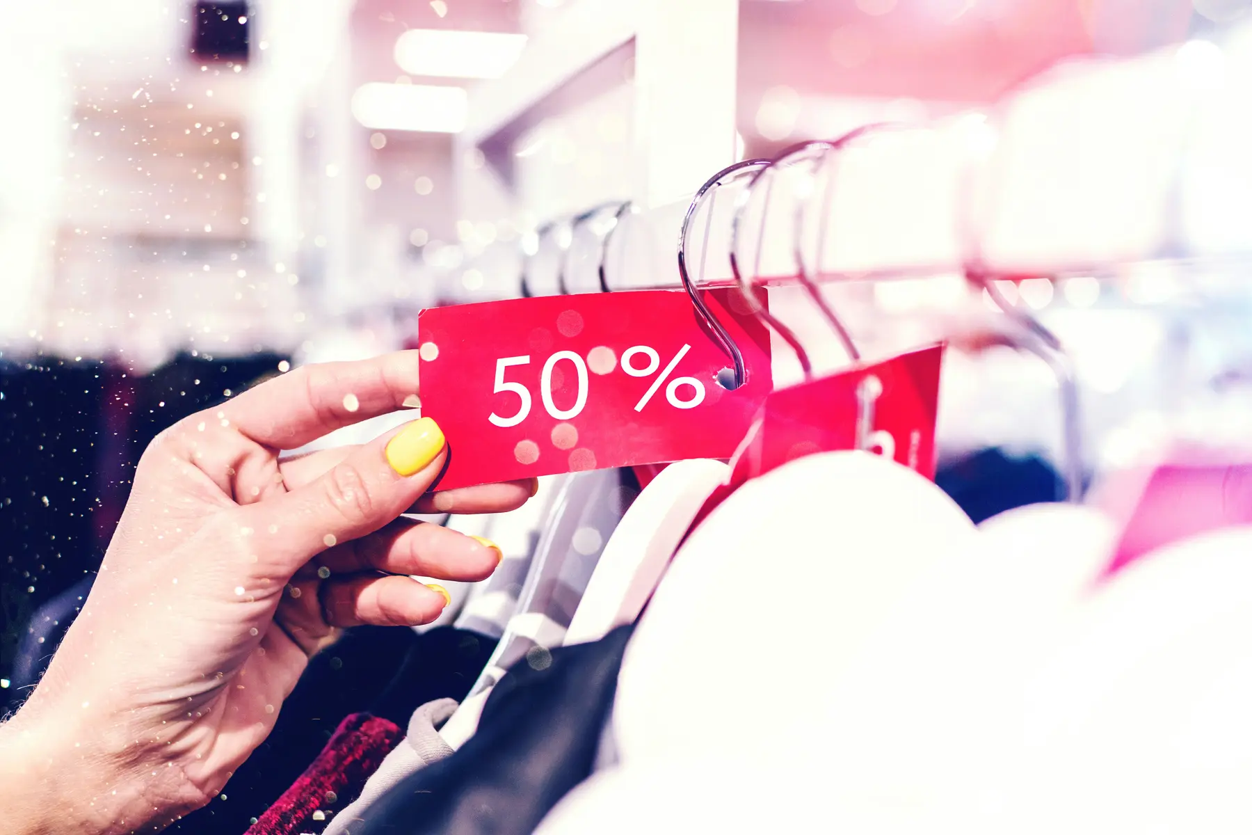 A hand holding a discount tag on a clothing rail, representing the offer and pricing behind a sale